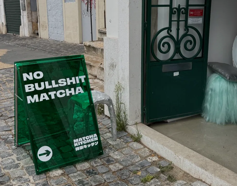 Green translucent acrylic pavement sandwich board sign on cobblestone street outside cafe entrance
