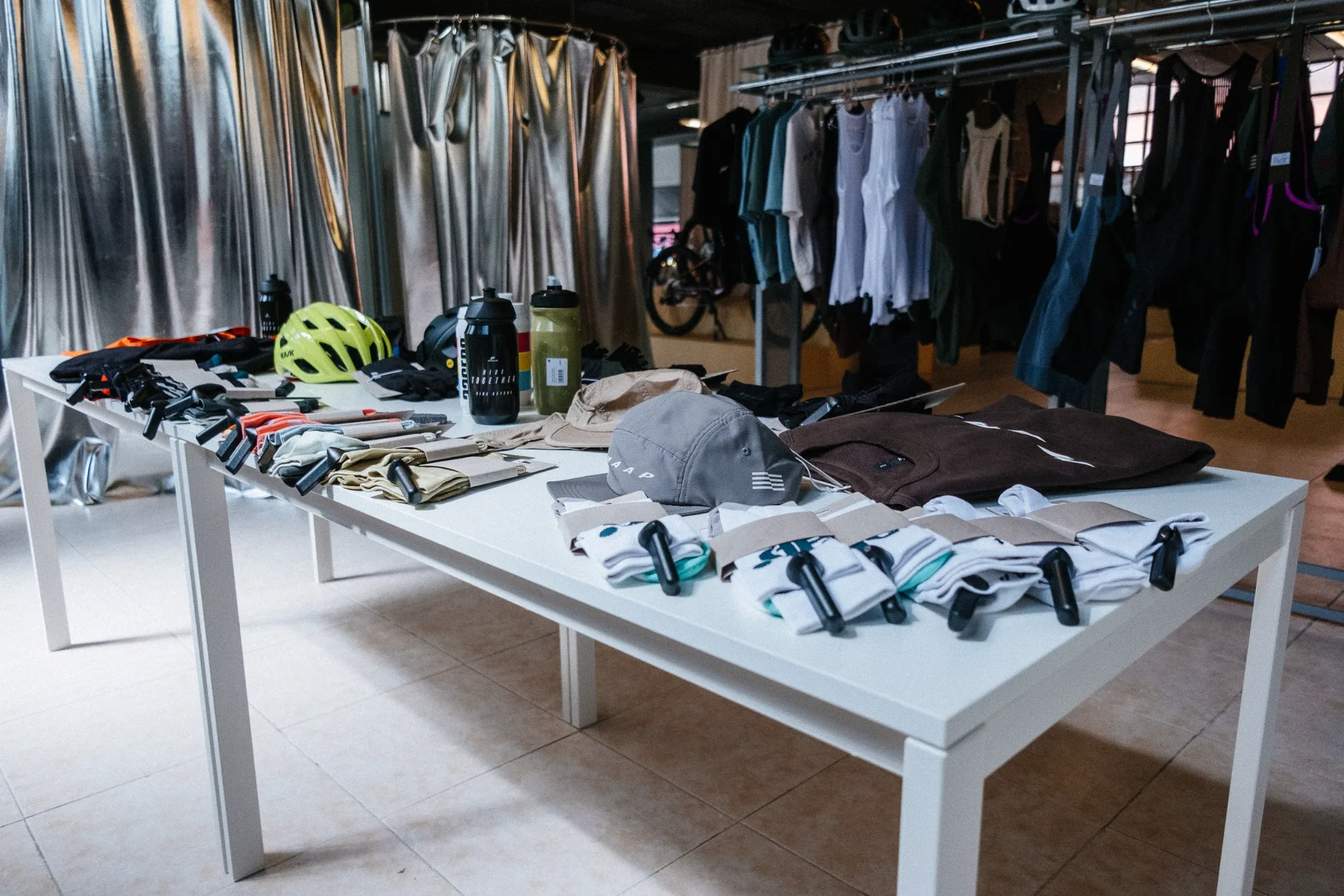 White display table with cycling accessories, helmets, and socks in front of a metallic curtain fitting room