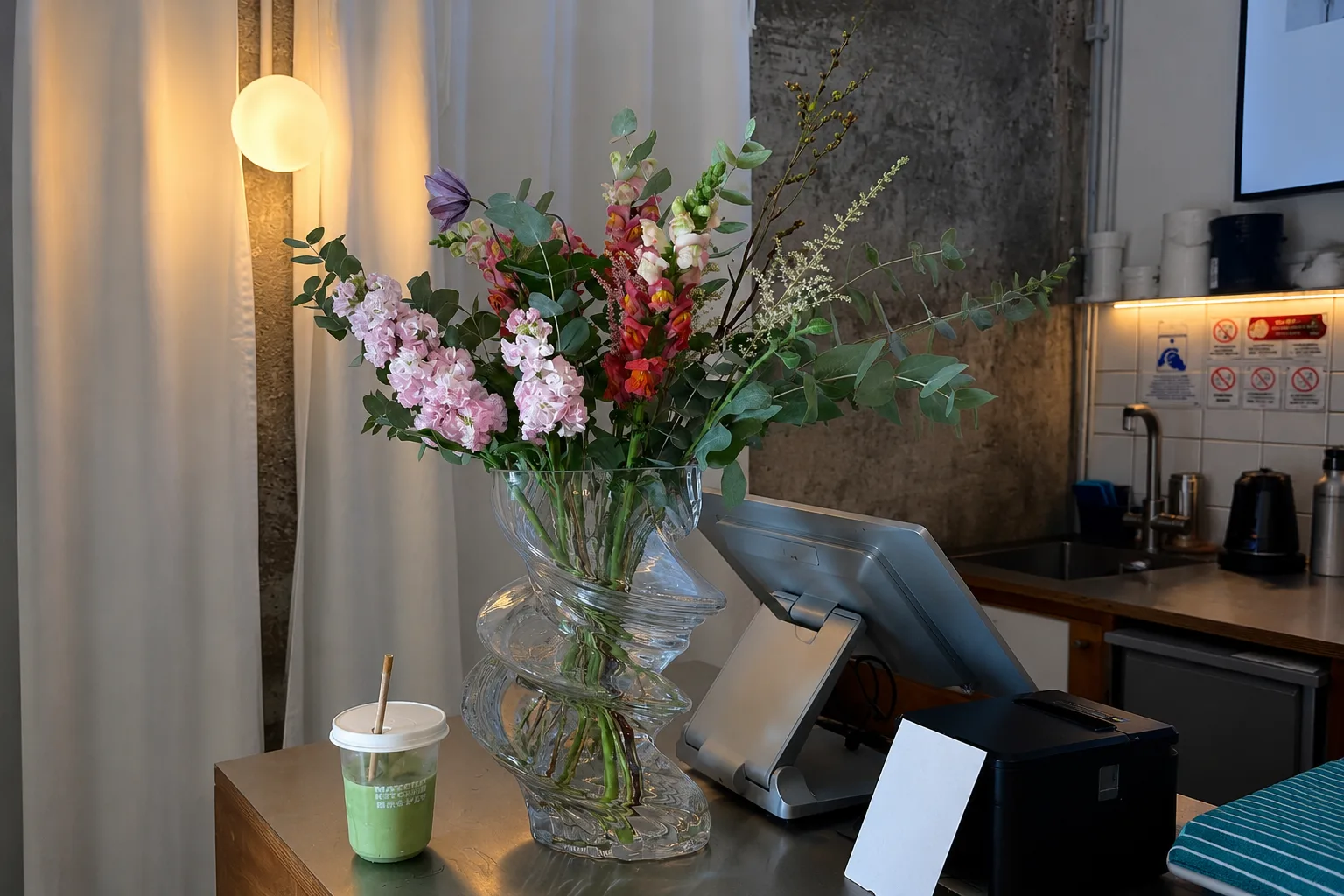 Matcha bar counter featuring fluted glass flower vase, iced matcha latte, and POS order terminal