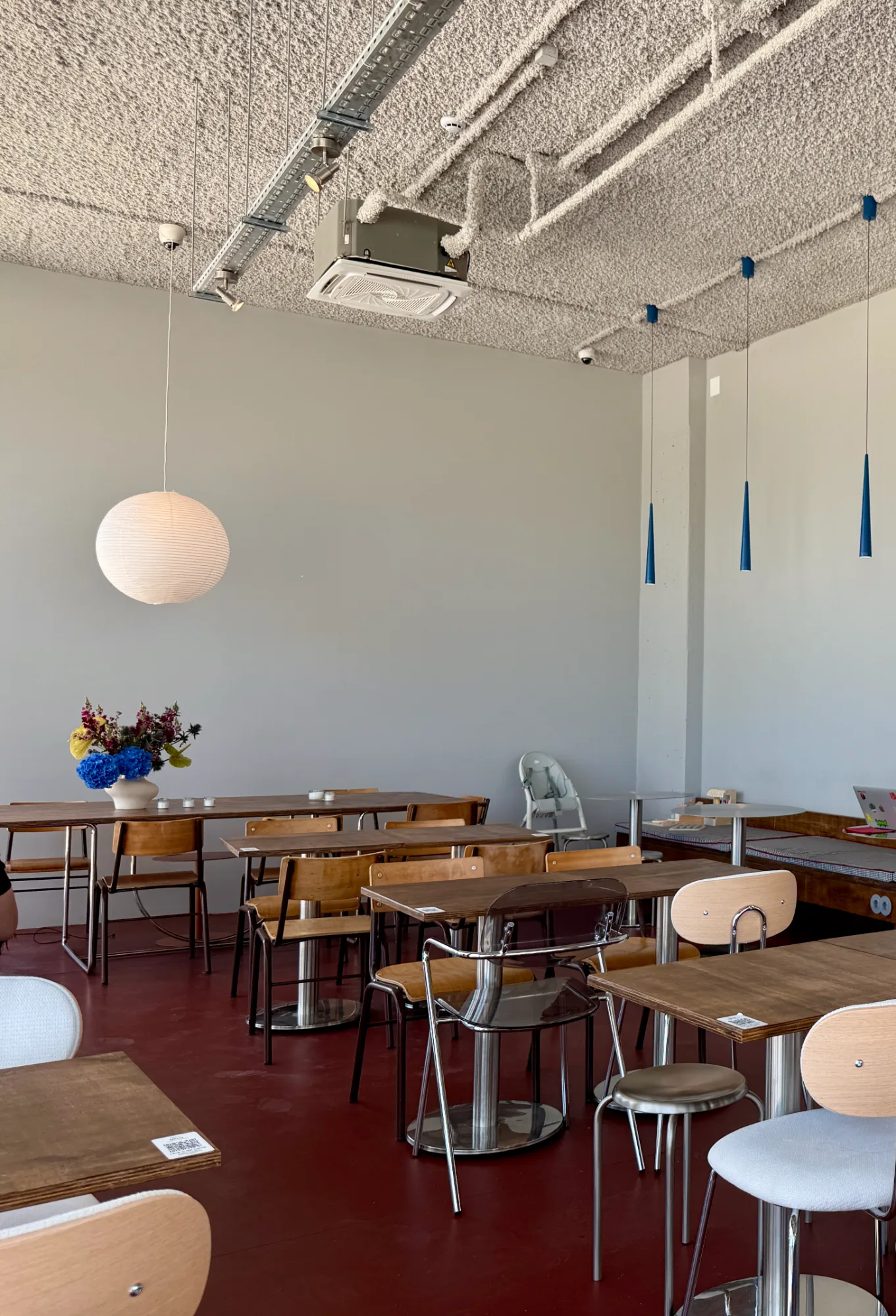 Cafe dining room with burgundy floor, wooden chairs, built-in wooden banquette bench, and blue pendant lights