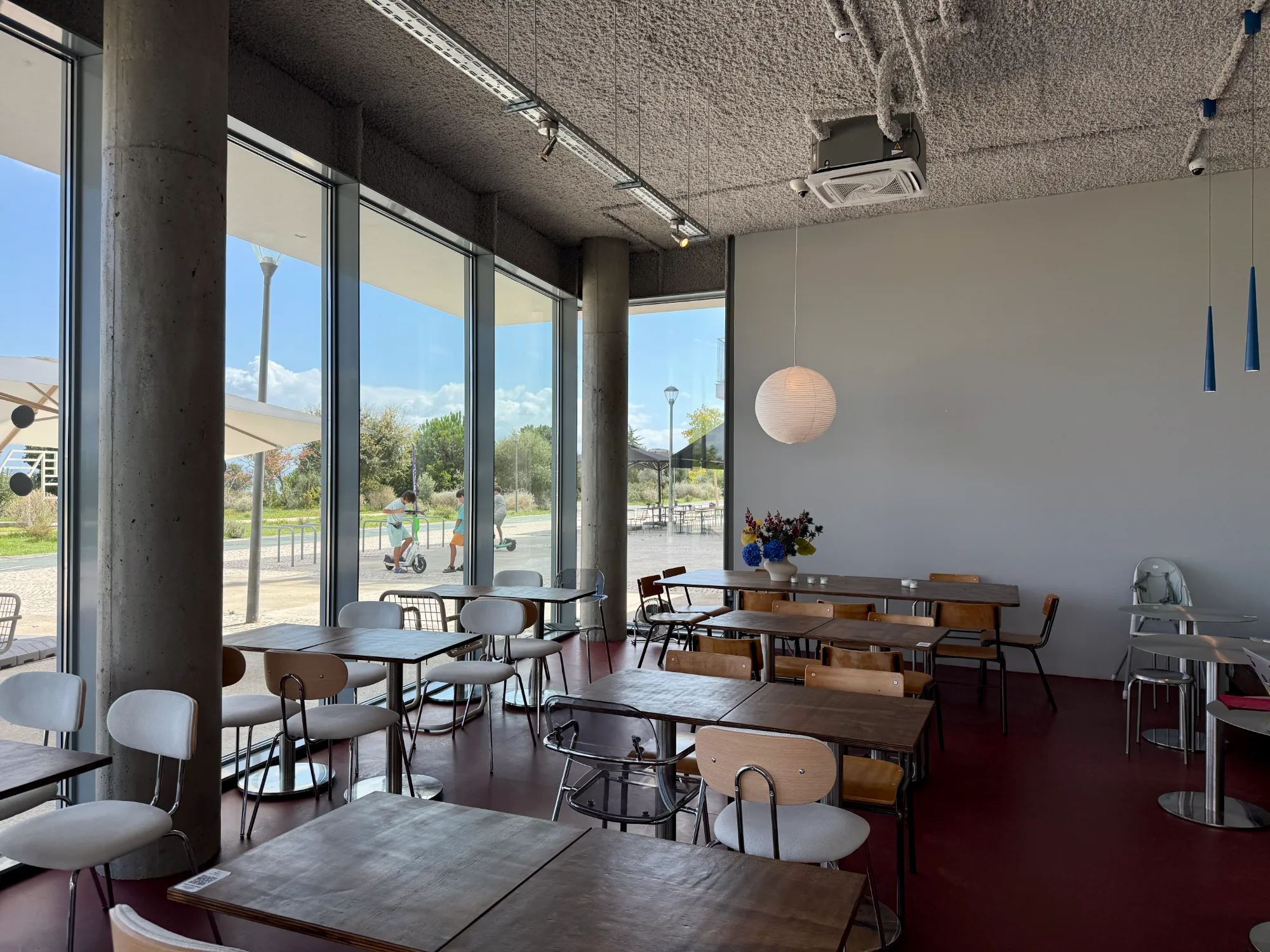 Cafe interior with floor-to-ceiling windows, exposed concrete columns, and mixed contemporary seating