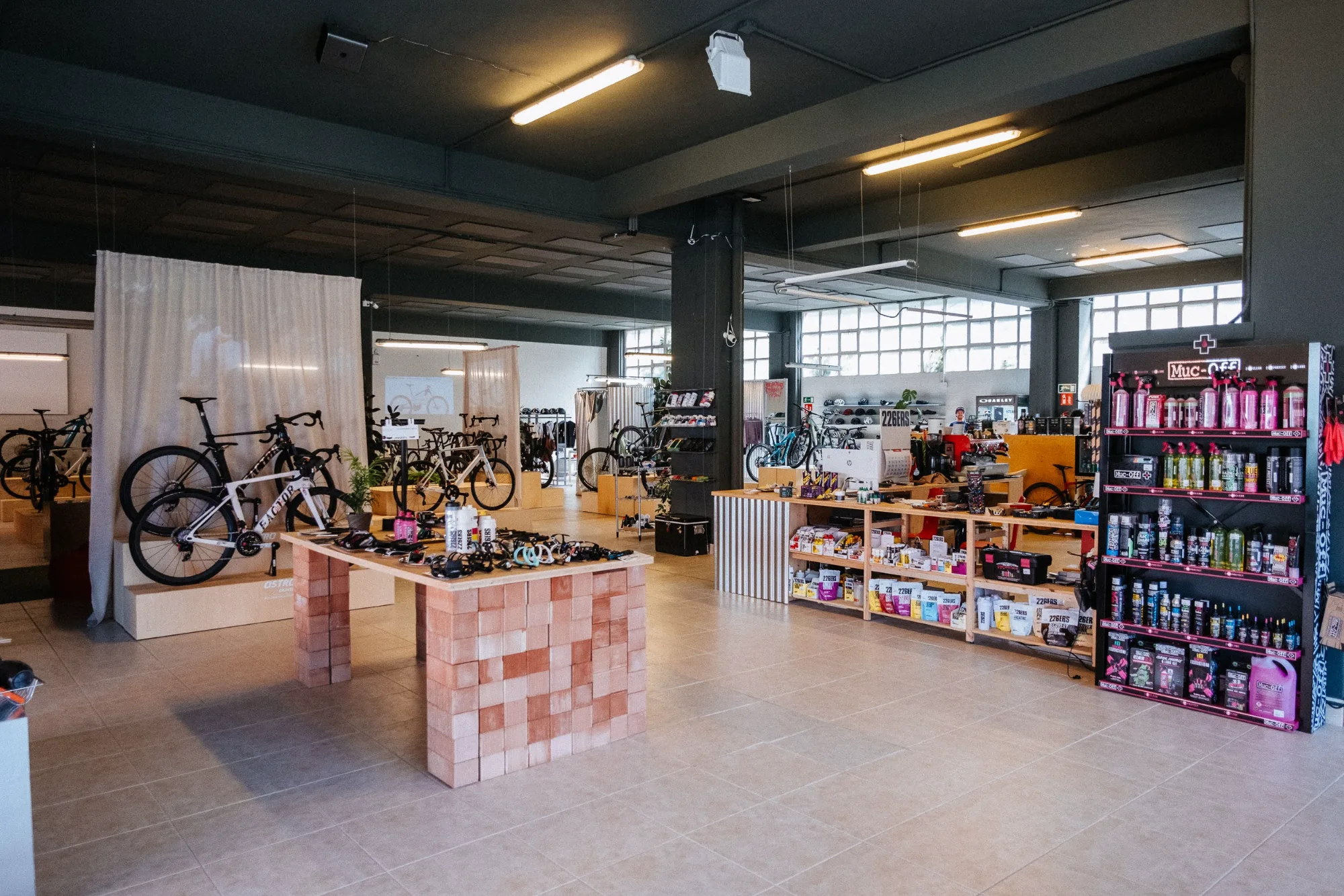 Bicycle shop interior featuring brick display table, modular plywood podiums, and open industrial ceiling