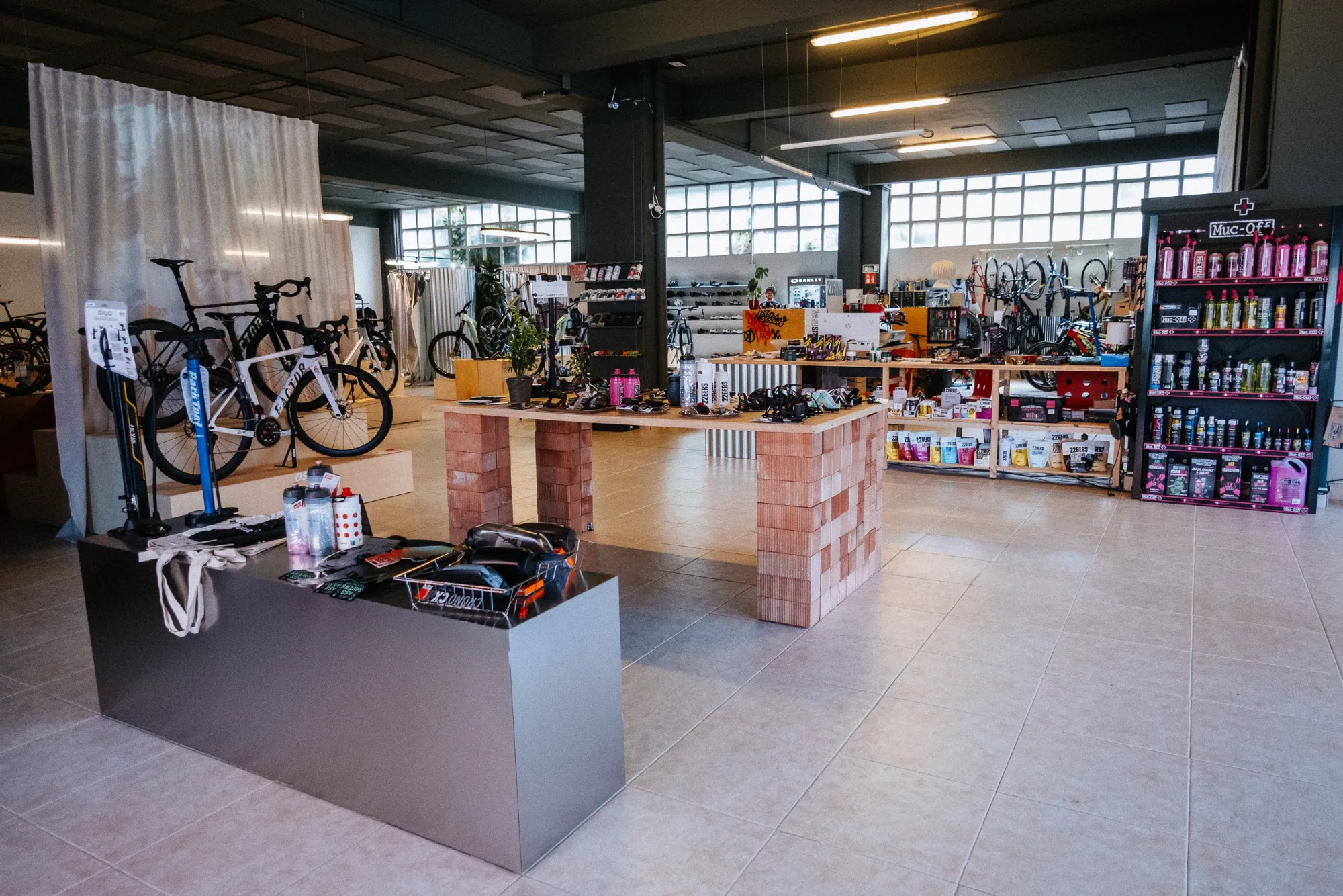 Retail showroom interior with metal display counter, terracotta brick table, and bicycles on wooden stages